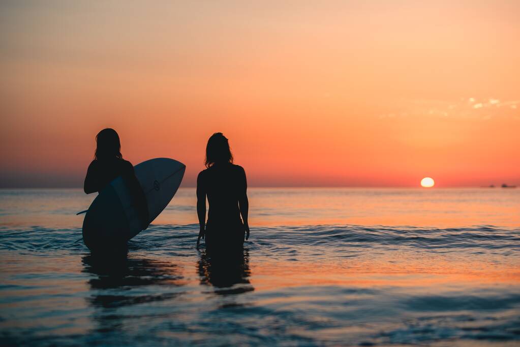Domburg, 29 jun 2019: Een prachtige opname van twee surfers die in het water staan te kijken naar de adembenemende zonsondergang - Foto, afbeelding