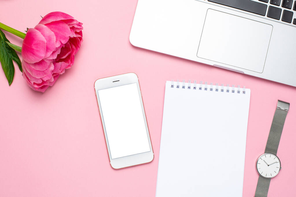 Мобильный телефон макет, ноутбук и пионерский цветок на розовом пастельном столе в плоском стиле. Рабочий стол
. - Фото, изображение