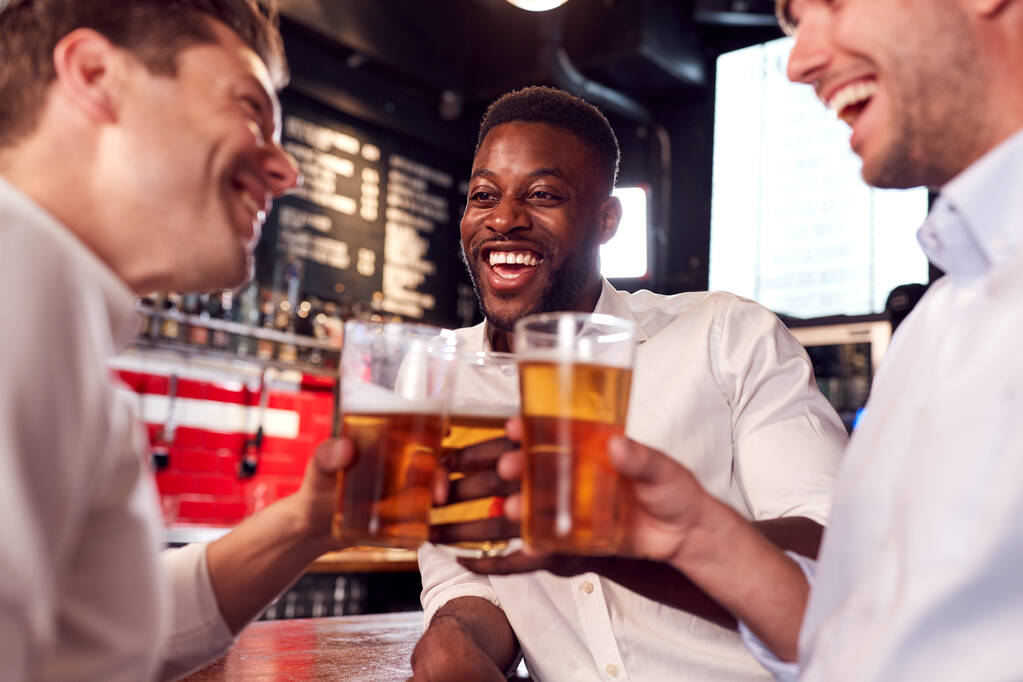 Kolme miestä tekee paahtoleipää, kun he tapaavat juomia ja seurustelevat baarissa töiden jälkeen
 - Valokuva, kuva