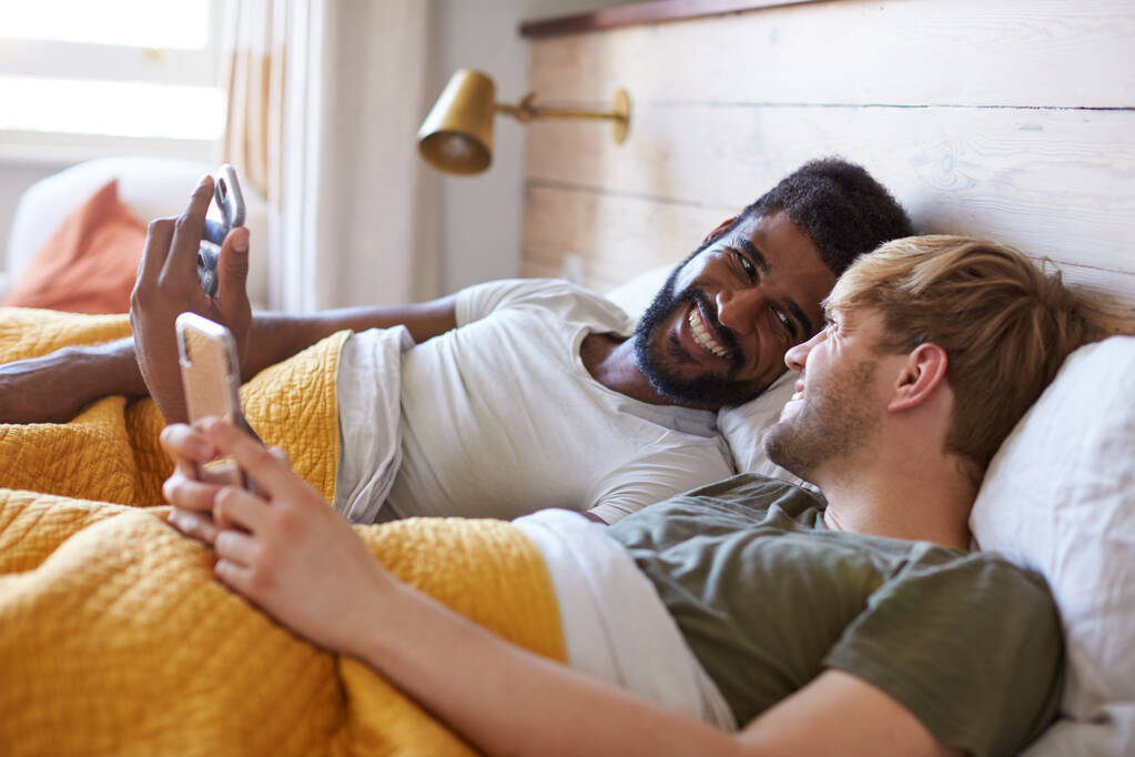 mâle gay couple allongé dans lit à la maison vérification téléphones mobiles ensemble
 - Photo, image