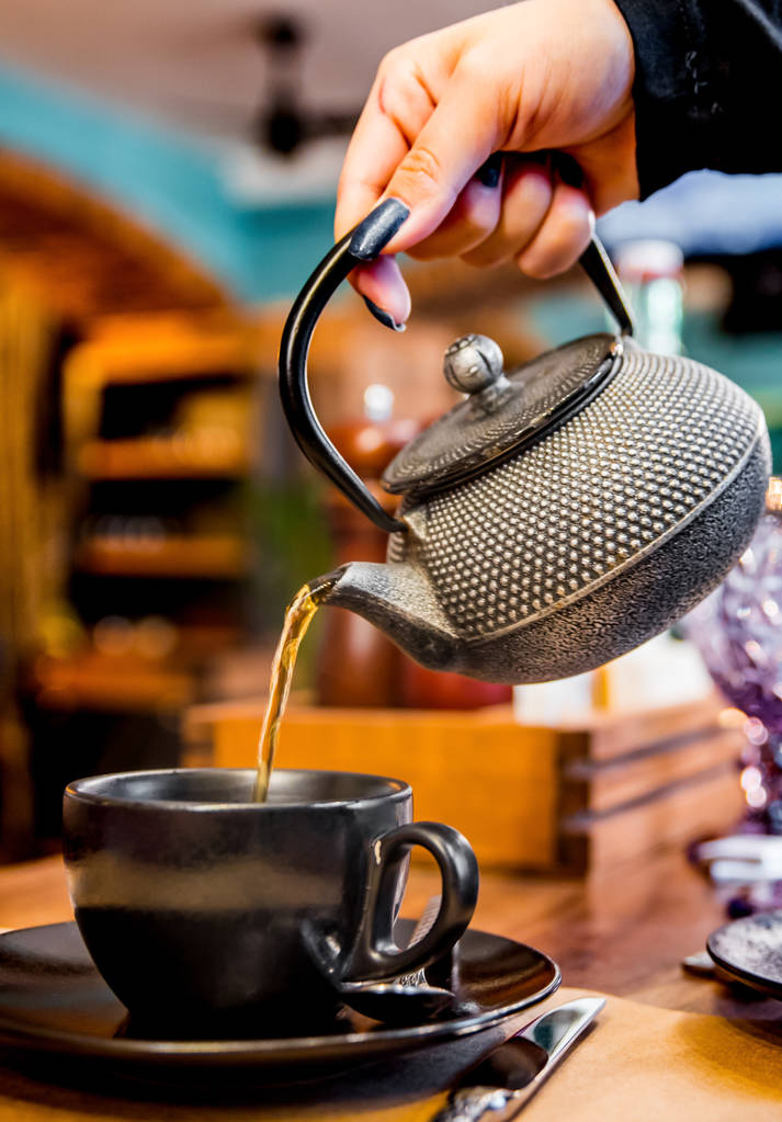 металевий чайник вливають чорний чай в чорний скляний кухоль в кафе
 - Фото, зображення