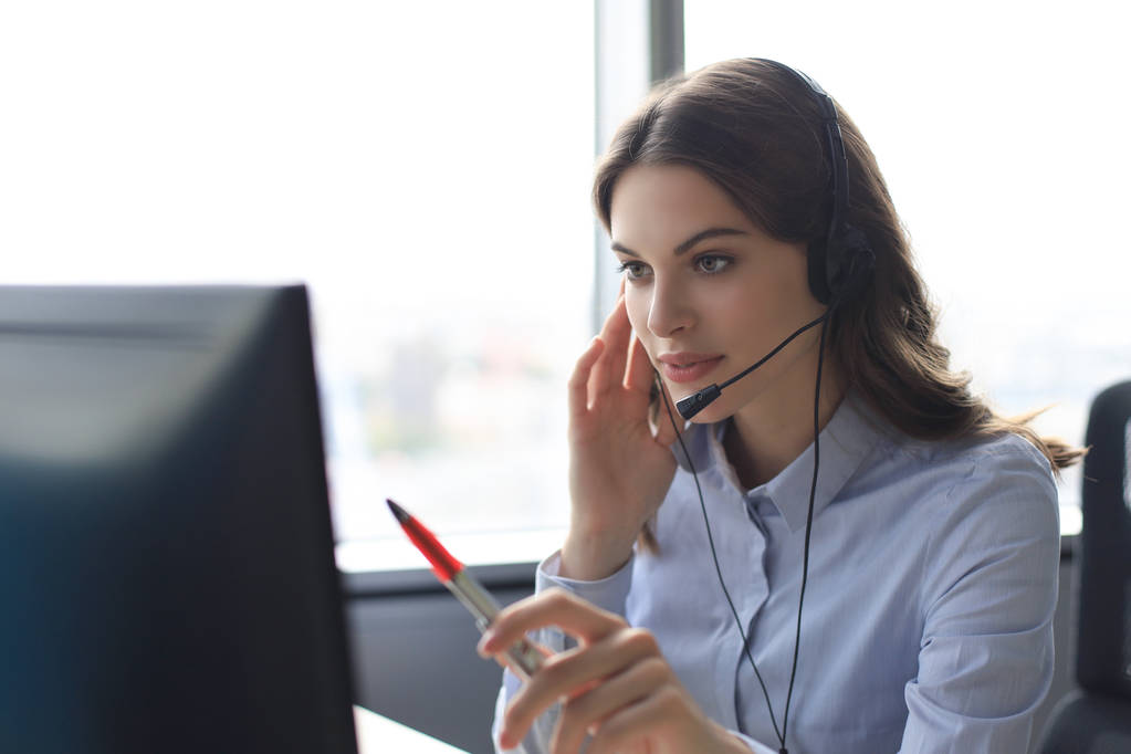 Krásná usmívající se call centrum pracovník ve sluchátkách pracuje v moderní kanceláři - Fotografie, Obrázek