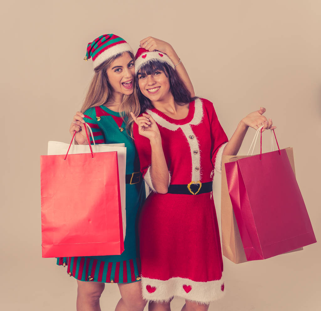 Podekscytowani nastolatkowie z torbami na zakupy kupując prezenty świąteczne w kapeluszu Mikołaja i zabawny strój świąteczny. Torby papierowe z miejscem na tekst. Ludzie, święta, świąteczne zakupy i czarny piątek. - Zdjęcie, obraz