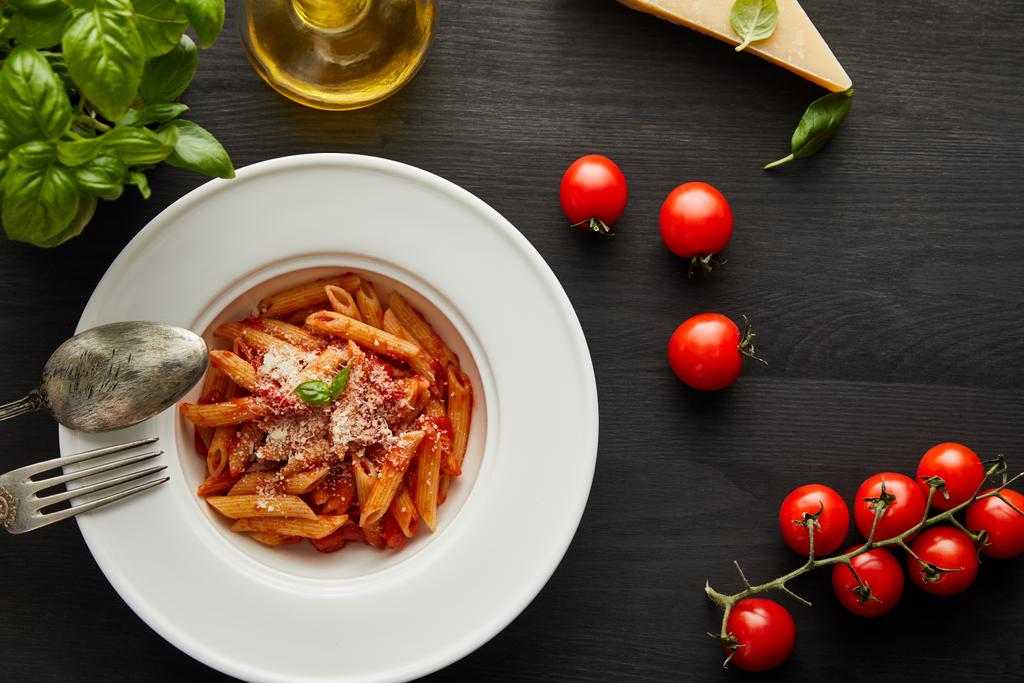 вид на вкусные болоньезе макароны с томатным соусом и пармезан в белой тарелке рядом с ингредиентами и столовыми приборами на черном деревянном фоне
 - Фото, изображение
