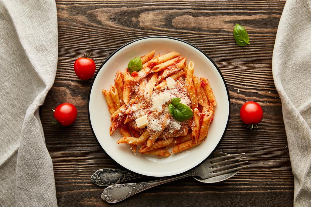 Draufsicht auf leckere Bolognese-Pasta mit Tomatensauce und Parmesan auf weißem Teller in der Nähe von Zutaten und Besteck auf Holztisch - Foto, Bild