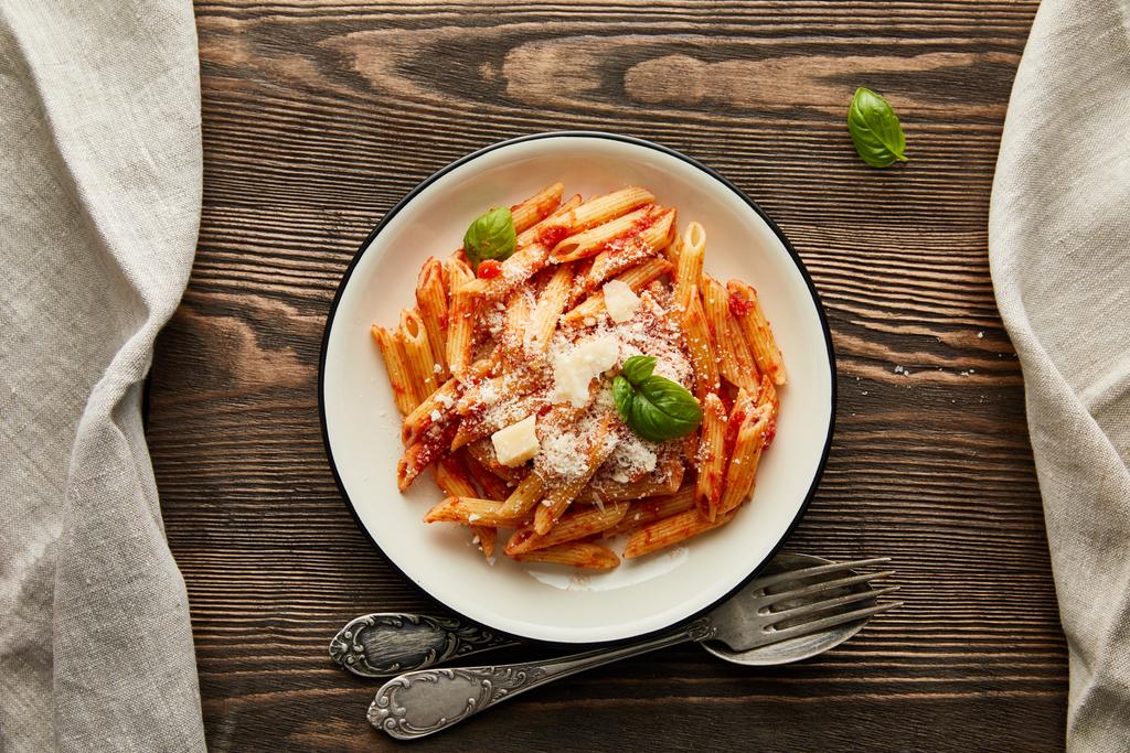 top view of tasty bolognese pasta with tomato sauce and Parmesan in white plate near cutlery on wooden background - Photo, Image