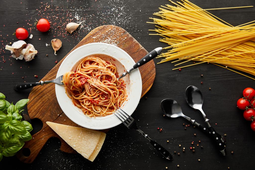 ylhäältä näkymä maukas bolognese pasta valkoinen levy lähellä ainesosia ja ruokailuvälineet musta puinen tausta
 - Valokuva, kuva