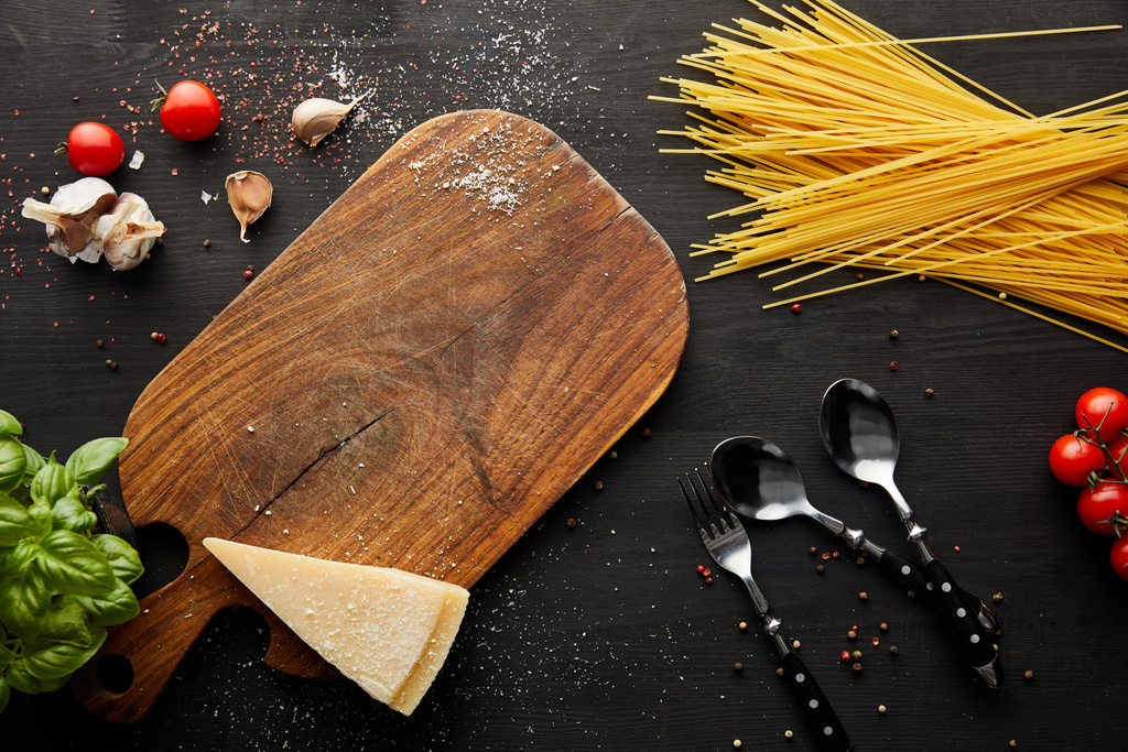 vrchní pohled na boloňské těstoviny ingredience, řezací deska a příbory na černém dřevěném pozadí - Fotografie, Obrázek
