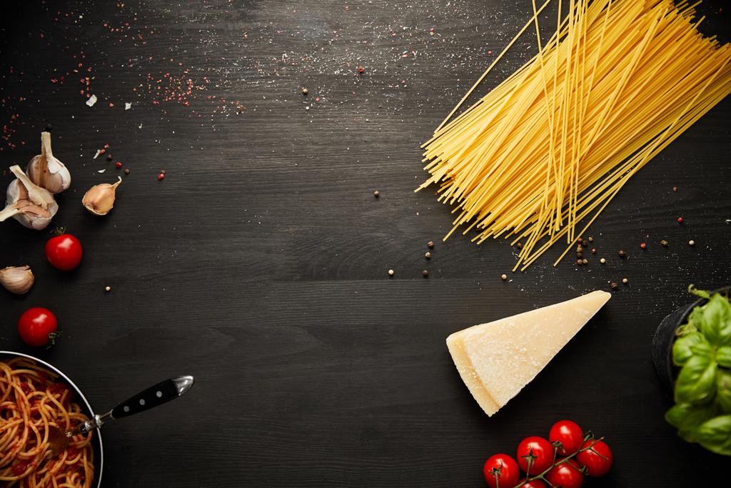 vista superior de la deliciosa pasta boloñesa en sartén cerca de los ingredientes sobre fondo de madera negro con espacio para copiar
 - Foto, Imagen