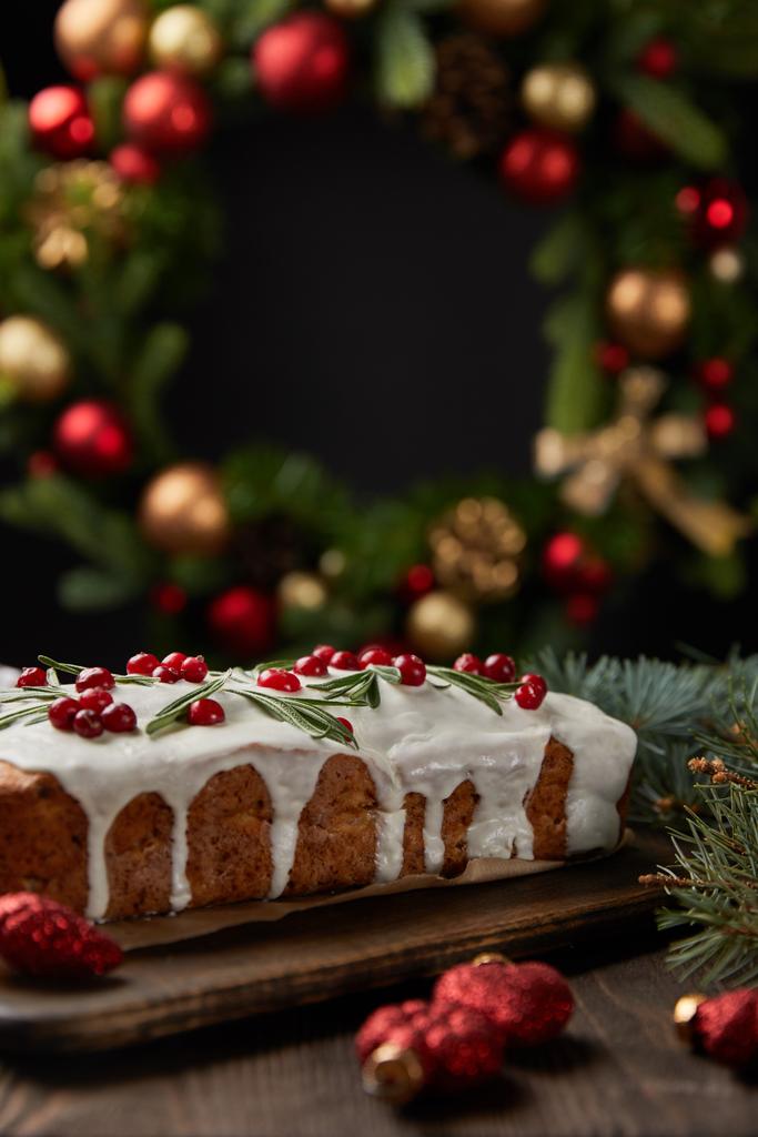 foyer sélectif de gâteau de Noël traditionnel avec canneberge près de couronne de Noël avec des boules sur table en bois isolé sur noir
 - Photo, image