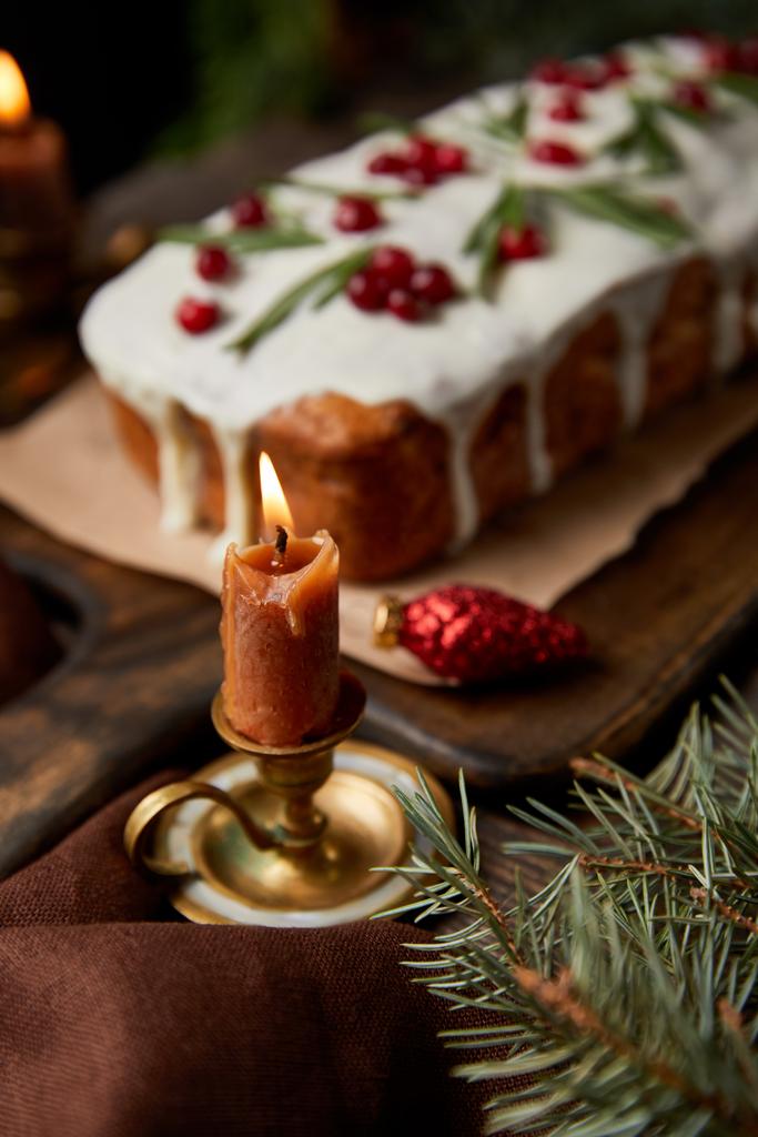 foco selectivo de pastel tradicional de Navidad con arándano cerca de la vela ardiente en la mesa de madera
 - Foto, imagen