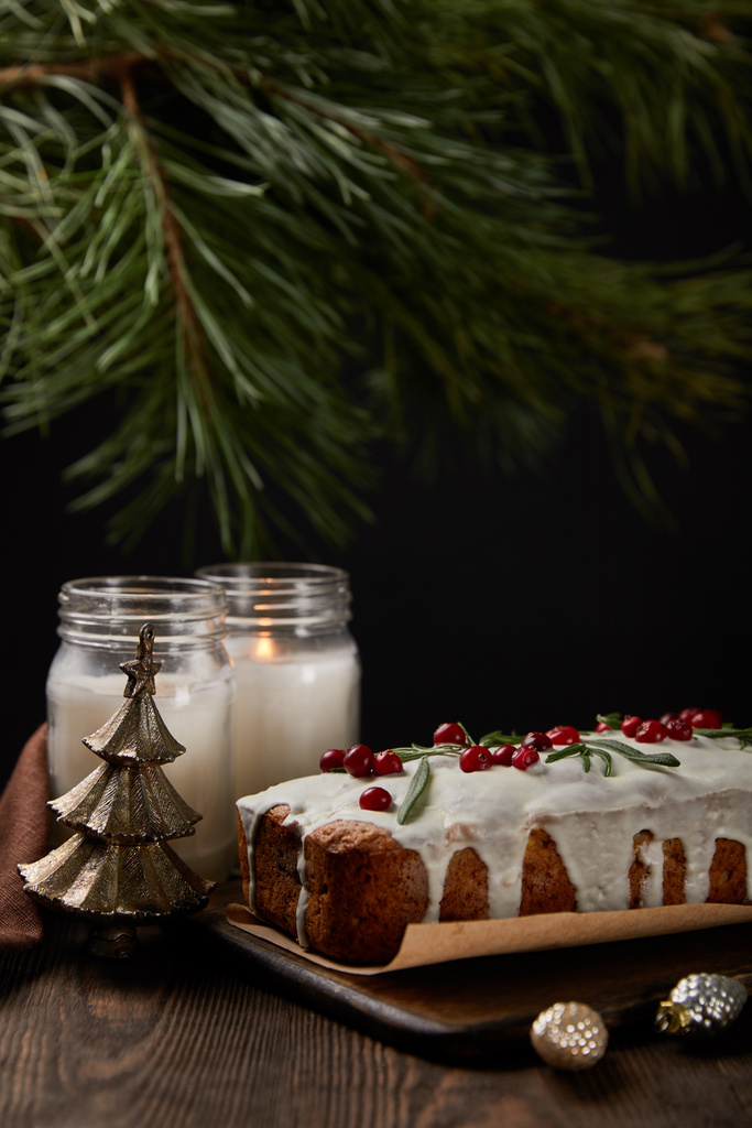 traditional Christmas cake with cranberry near pine, baubles and candles on wooden table - Photo, Image