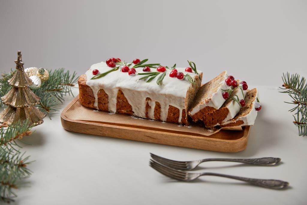 traditionele kerstcake met cranberry bij vorken, kerstballen en dennen op witte tafel geïsoleerd op grijs - Foto, afbeelding