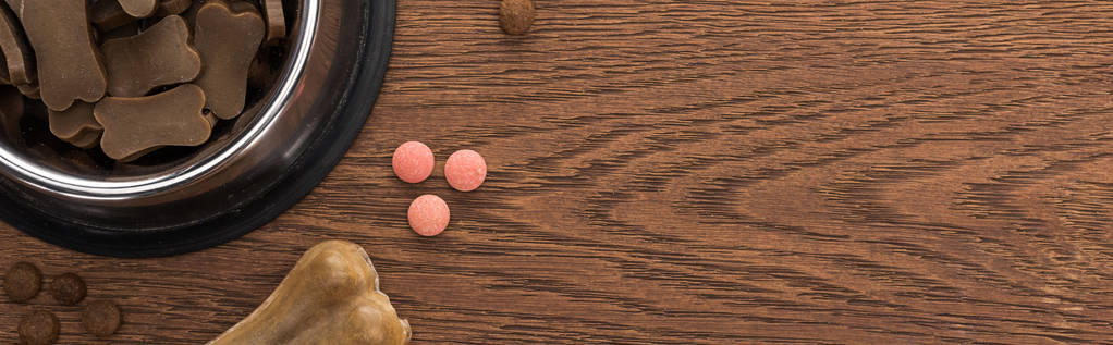 vue du dessus de la nourriture sèche pour animaux de compagnie dans un bol en argent près des os et des vitamines roses sur une table en bois, vue panoramique
 - Photo, image