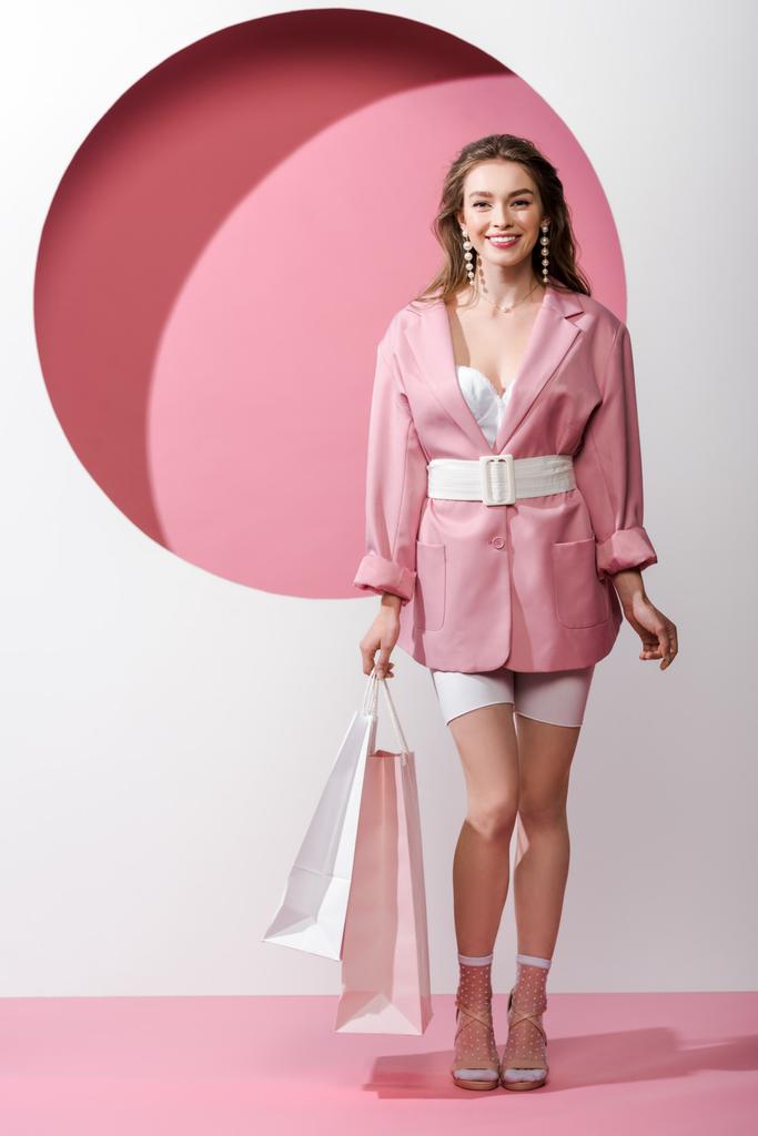 fröhliches und stilvolles Mädchen mit Einkaufstaschen in weiß und rosa  - Foto, Bild