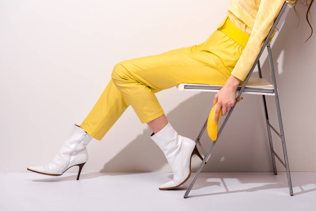 vista recortada de la mujer sentada en la silla y sosteniendo plátano amarillo en blanco
  - Foto, imagen