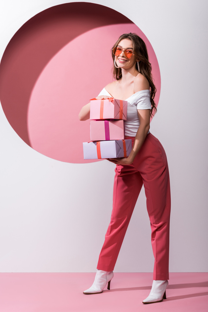 happy woman holding presents while standing on pink and white  - Photo, Image