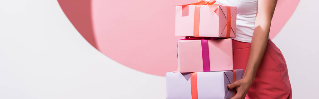 prise de vue panoramique de femme tenant des cadeaux tout en se tenant debout sur rose et blanc
  - Photo, image