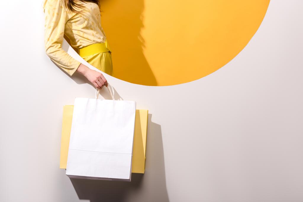 καλλιεργημένη άποψη της νεαρής γυναίκας που κρατά σακούλες για ψώνια σε πορτοκαλί και άσπρο  - Φωτογραφία, εικόνα