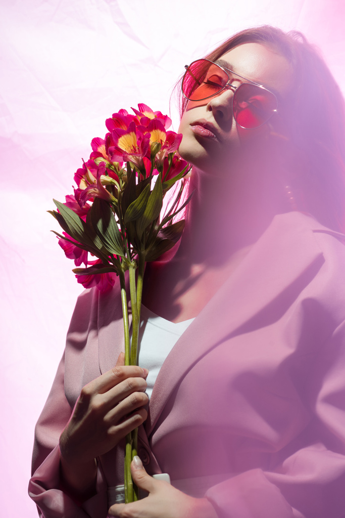 aantrekkelijke vrouw in zonnebril houden bloemen op wit - Foto, afbeelding