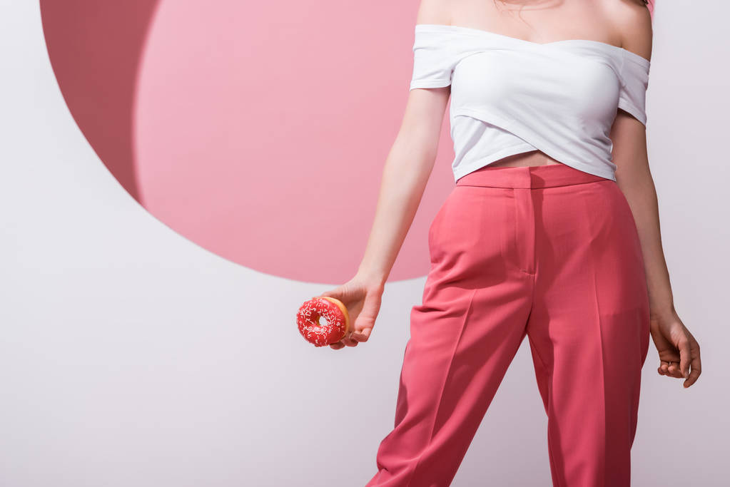 cropped view of woman holding doughnut on pink and white  - 写真・画像