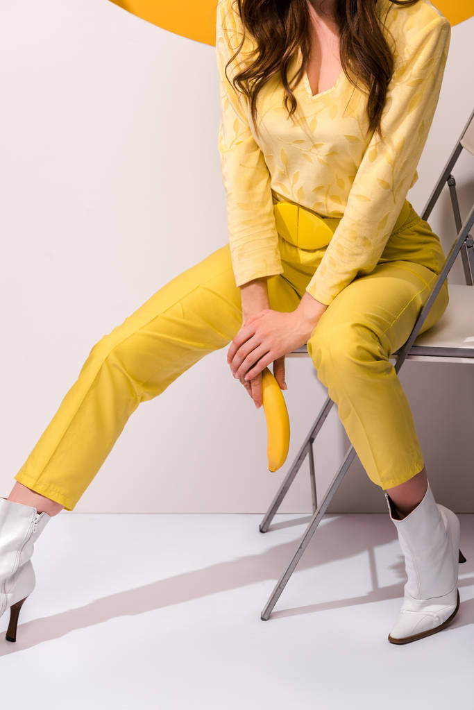 vue recadrée de la femme assise sur la chaise et tenant banane sur blanc et orange
 - Photo, image