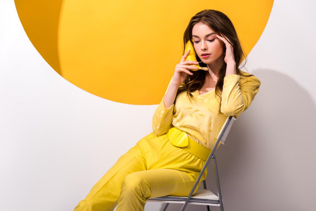 молода жінка сидить на стільці і тримає банан на білому і помаранчевому
 - Фото, зображення