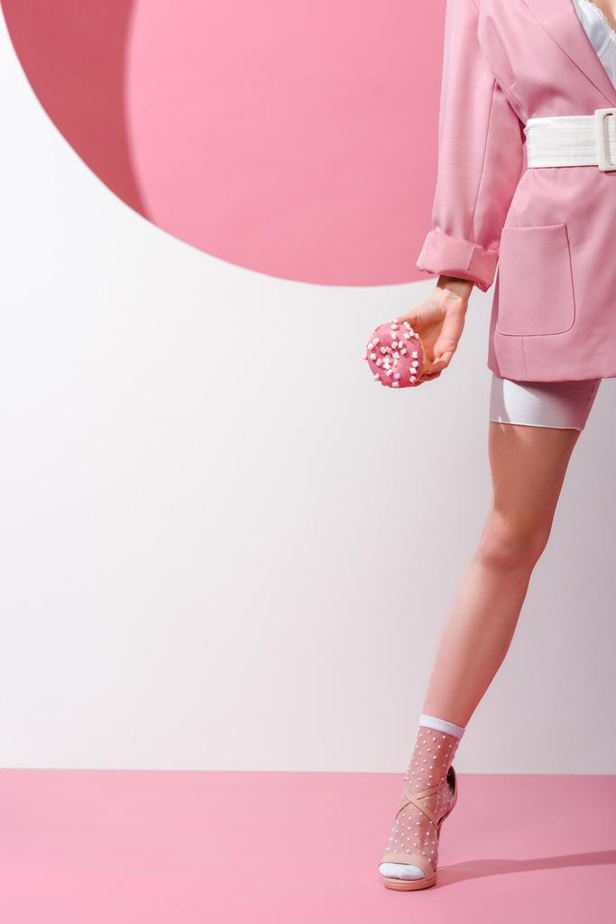 обрезанный вид женщины, стоящей и держащей сладкий пончик на розовом и белом
  - Фото, изображение