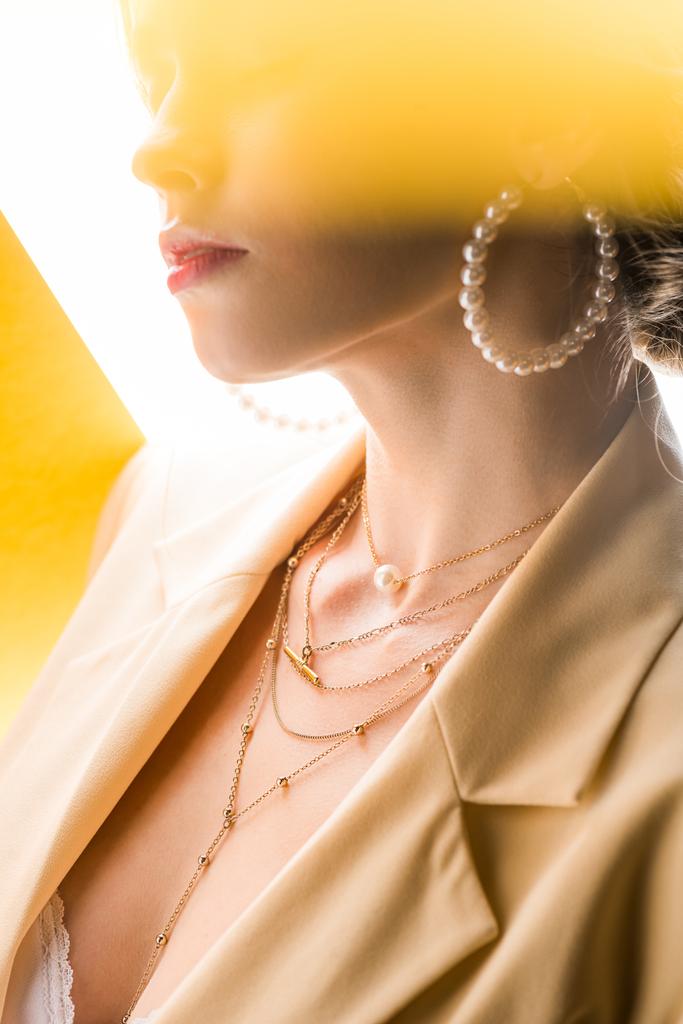 cropped view of young woman in necklace and earrings on orange and white  - 写真・画像