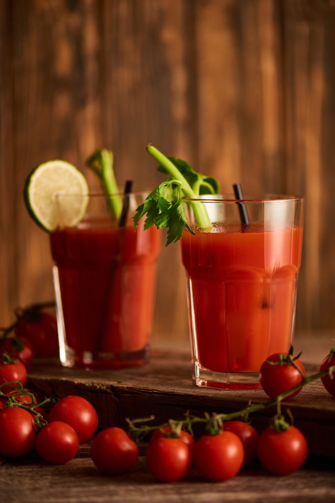 selektivní zaměření Bloody Mary koktejl v brýlích s limetkou a celerem na dřevěném pozadí s rajčaty - Fotografie, Obrázek