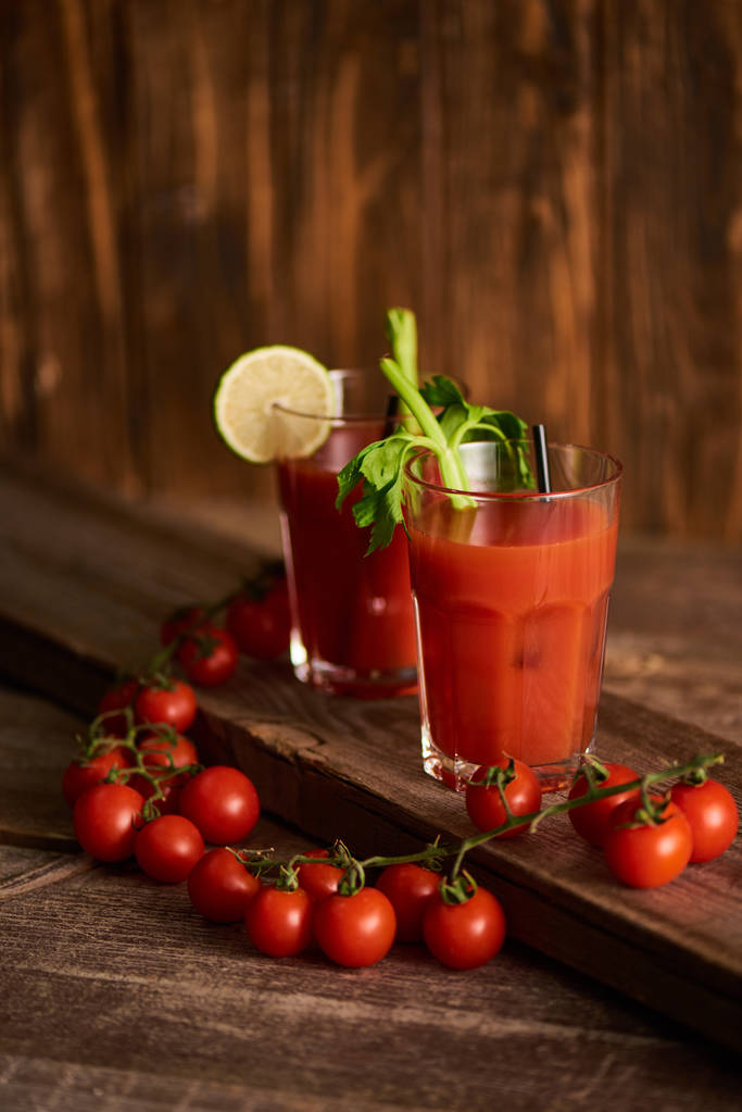 bloody mary cocktail in glasses with lime and celery on wooden background with tomatoes - Photo, Image