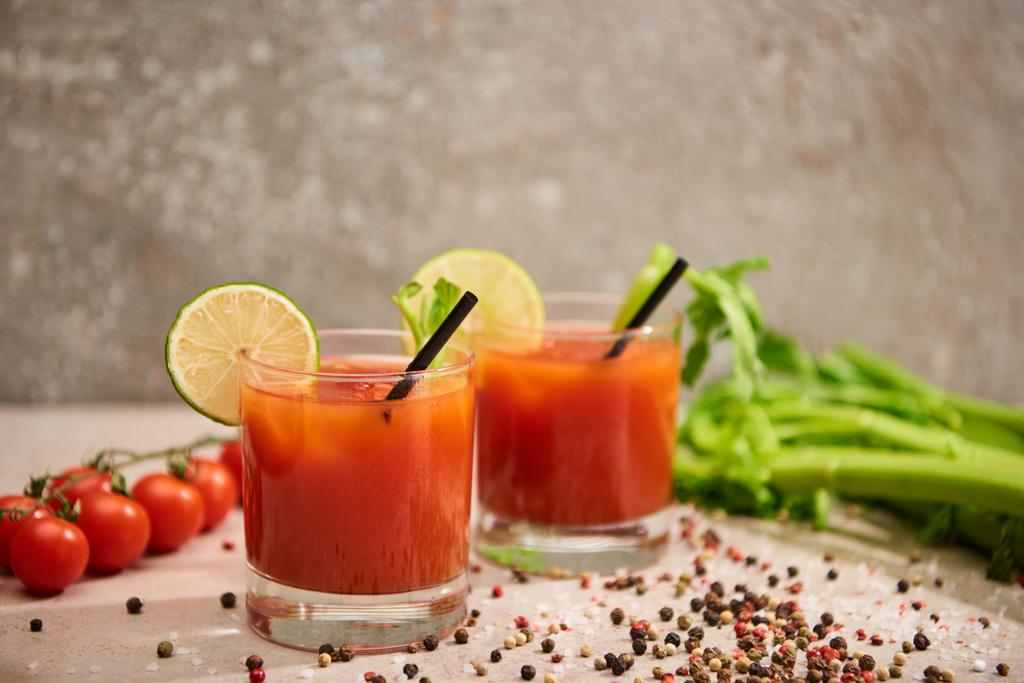 Bloody Mary cocktail in glazen met rietjes en limoen bij zout, peper, tomaten en selderij op grijze ondergrond - Foto, afbeelding