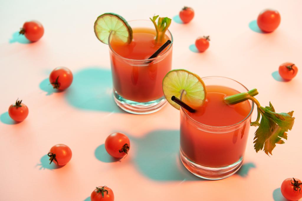 Bloody Mary cocktail in glazen versierd met limoen en selderij op een verlichte achtergrond met tomaten - Foto, afbeelding