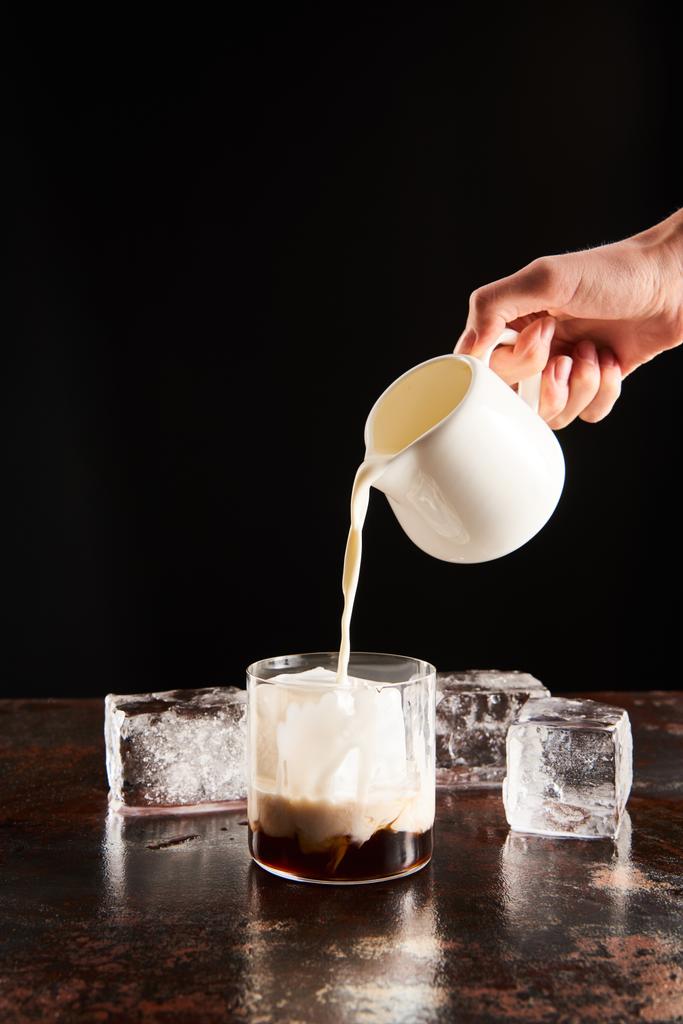 przycięty widok kobiety poring mleka w szkle z kostkami lodu izolowane na czarno - Zdjęcie, obraz
