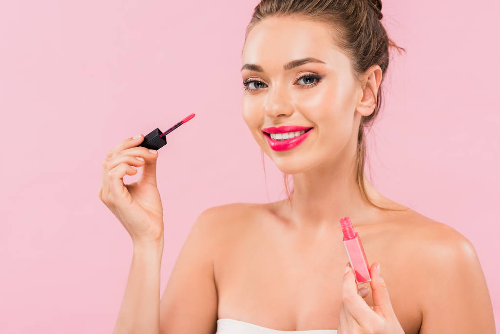 smiling naked beautiful woman with pink lips holding lip gloss isolated on pink  - Photo, Image