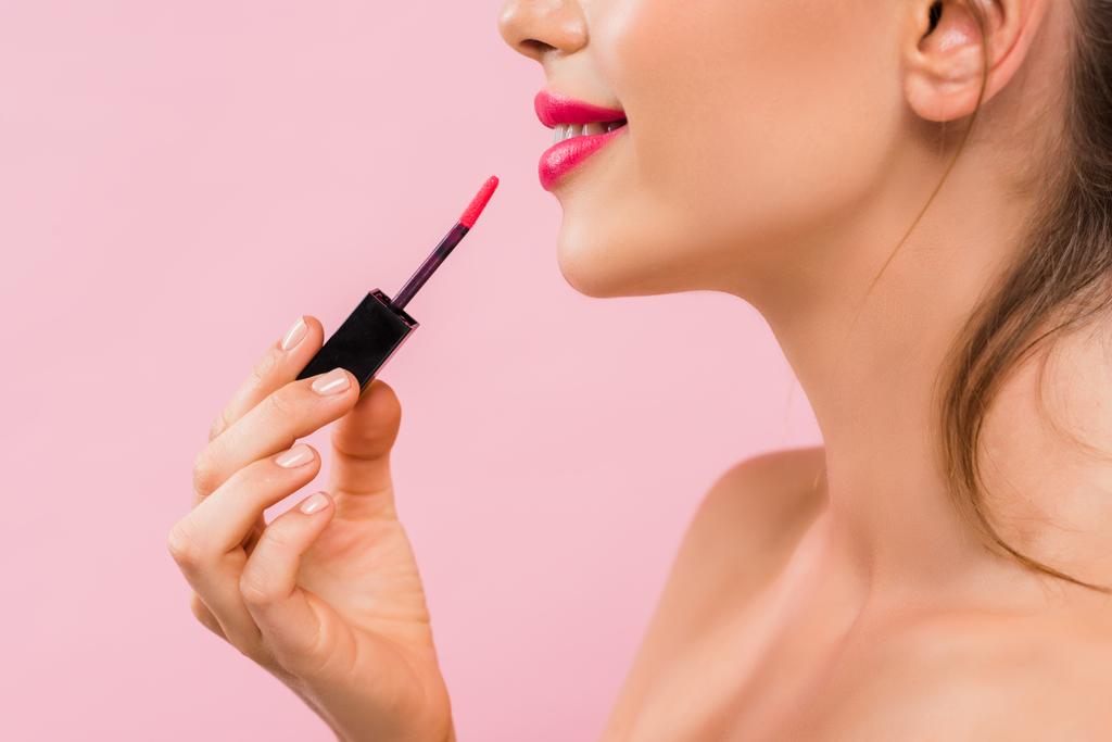 καλλιεργημένη άποψη του χαμόγελου γυμνή όμορφη γυναίκα με ροζ χείλη εφαρμογή lip gloss απομονώνονται σε ροζ  - Φωτογραφία, εικόνα