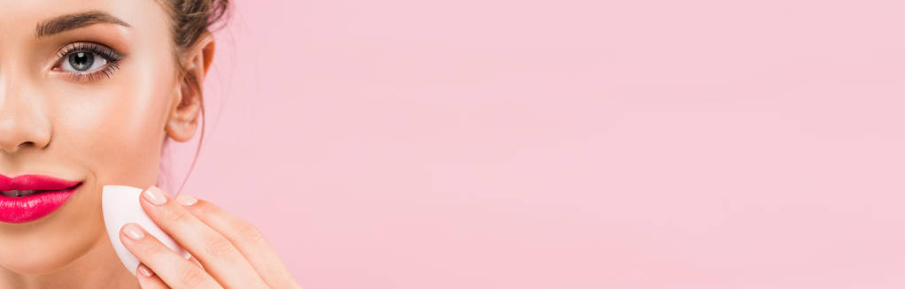 Pembe dudaklı çıplak güzel bir kadın pembe panoramik bir karede izole edilmiş makyaj süngeri tutuyor. - Fotoğraf, Görsel