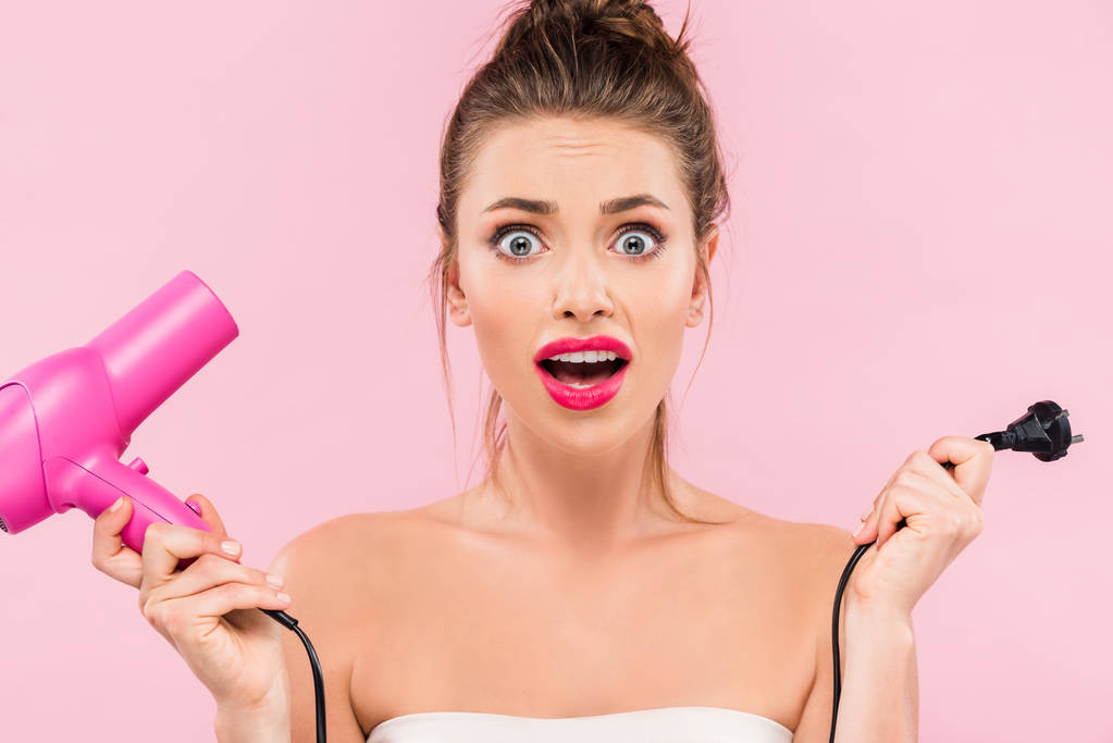 impactado hermosa mujer con labios rosados sosteniendo secador de pelo aislado en rosa
  - Foto, imagen