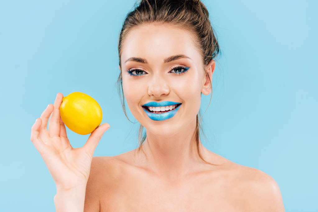 gelukkig naakt mooi vrouw met blauwe lippen houden geheel oranje geïsoleerd op blauw - Foto, afbeelding