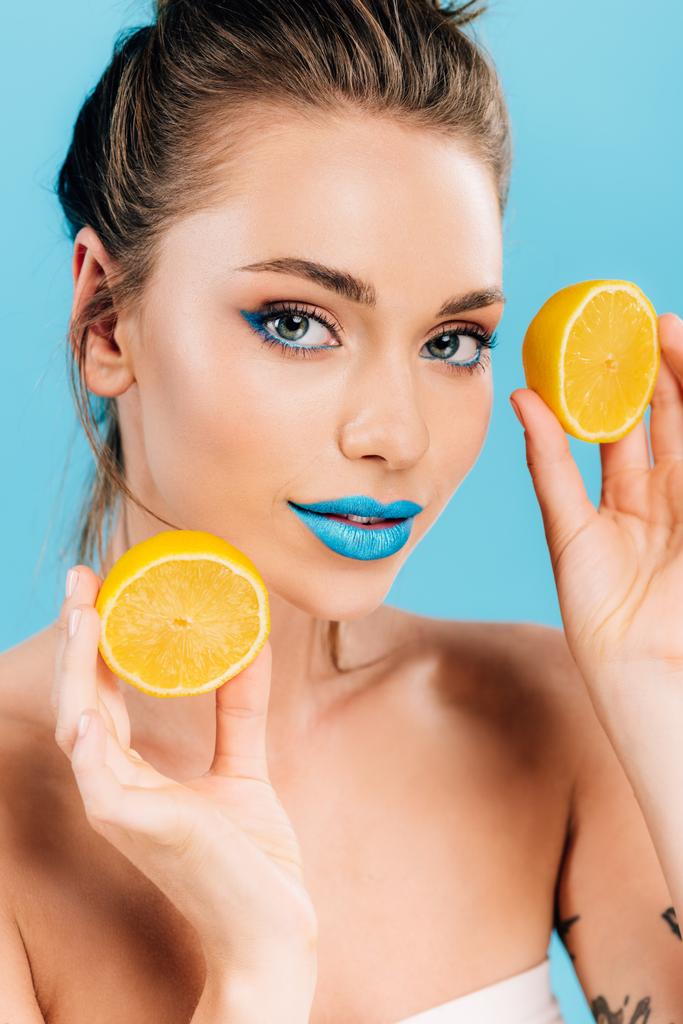 mujer hermosa desnuda con labios azules sosteniendo mitades anaranjadas aisladas en azul
 - Foto, Imagen