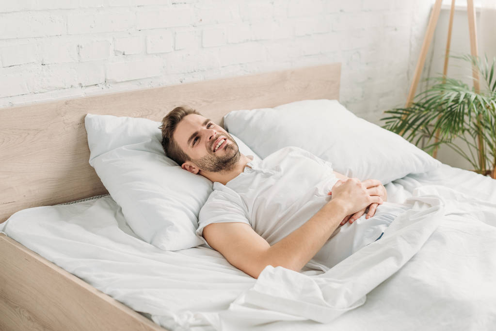 νεαρός άνδρας ξαπλωμένος στο κρεβάτι και πάσχοντας από κοιλιακό άλγος - Φωτογραφία, εικόνα