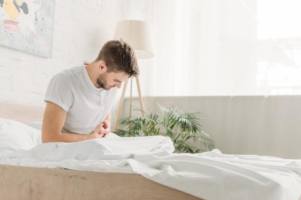 fiatal férfi ül az ágyban, és szenved hasi fájdalom - Fotó, kép