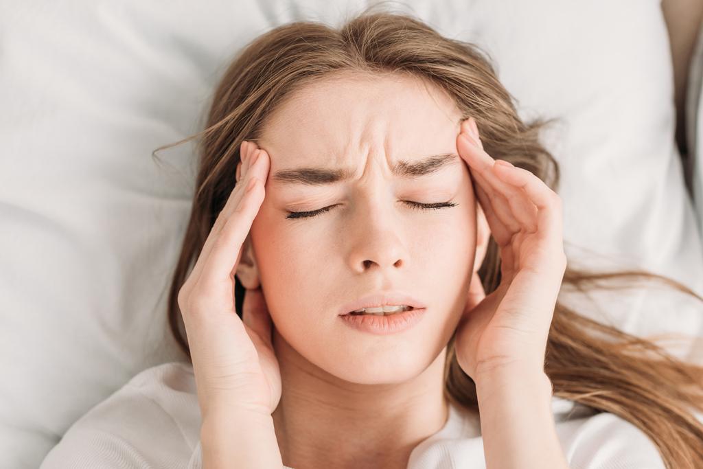 widok z góry młoda kobieta z zamkniętymi oczami dotykając głowy podczas gdy cierpi na migrenę - Zdjęcie, obraz