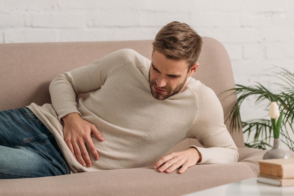 Junger Mann liegt auf Sofa und leidet unter Bauchschmerzen - Foto, Bild