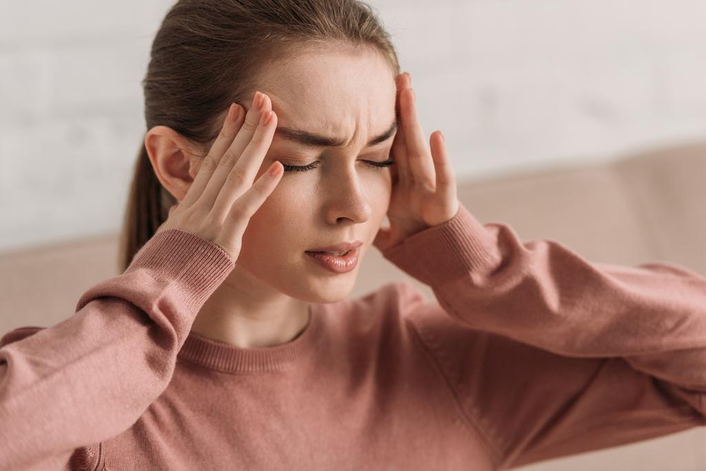 junge Frau hält Hände in Kopfnähe, während sie an Migräne mit geschlossenen Augen leidet - Foto, Bild