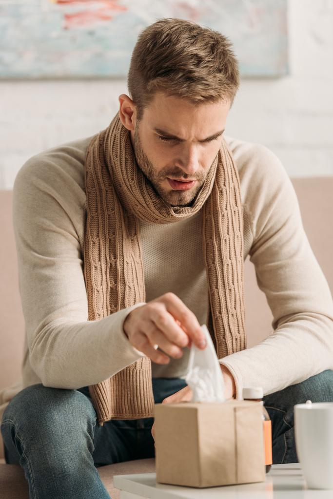 хворий чоловік у теплому шарфі бере серветку з пачки
 - Фото, зображення