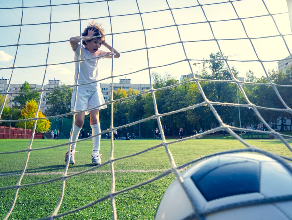 Мальчик или ребенок играет в футбол или футбол для упражнений и деятельности. Вид из-за сетки ворот. селективный фокус
 - Фото, изображение