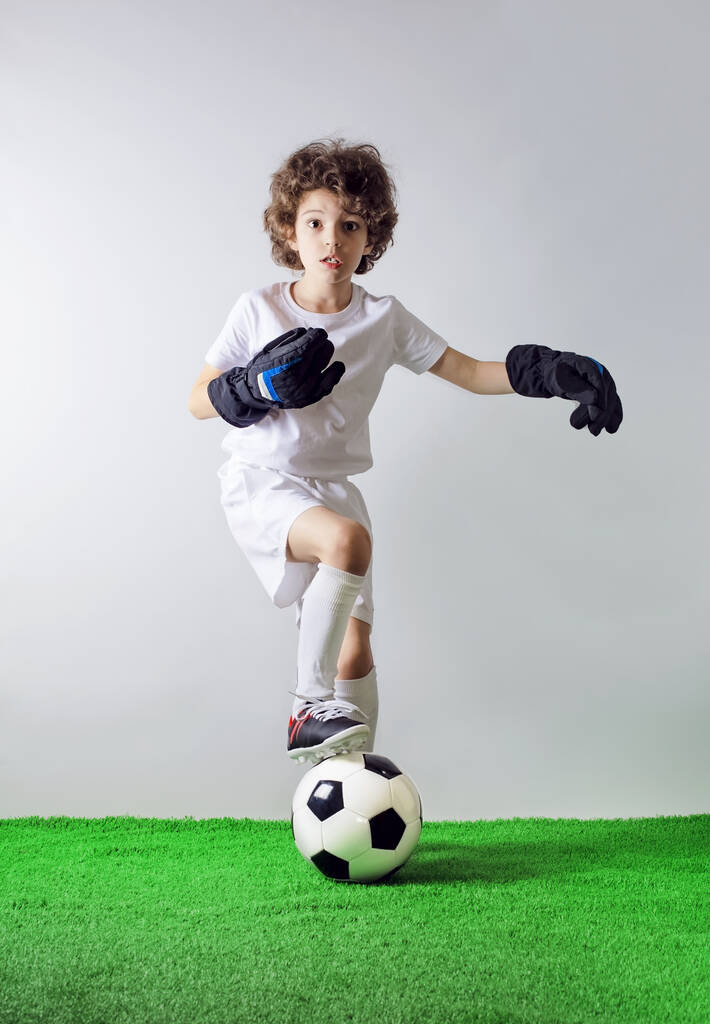 Handsome little football player with surprise facial expression. You talking to me. Little boy goalkeeper in white uniform pointing to himself with question if he did something wrong - Photo, Image