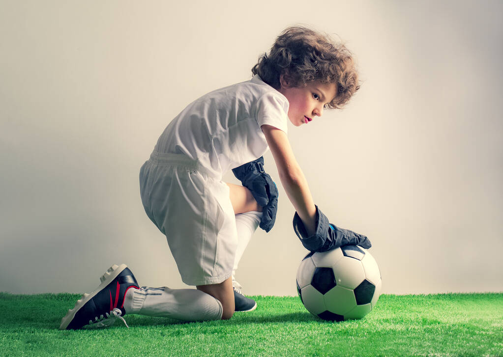 Футбольні заняття для дітей. Портрет милого потворного хлопця з футбольним м'ячем піднімається, щоб перейти на трав'яне студійне тло. Молодий воротар - Фото, зображення