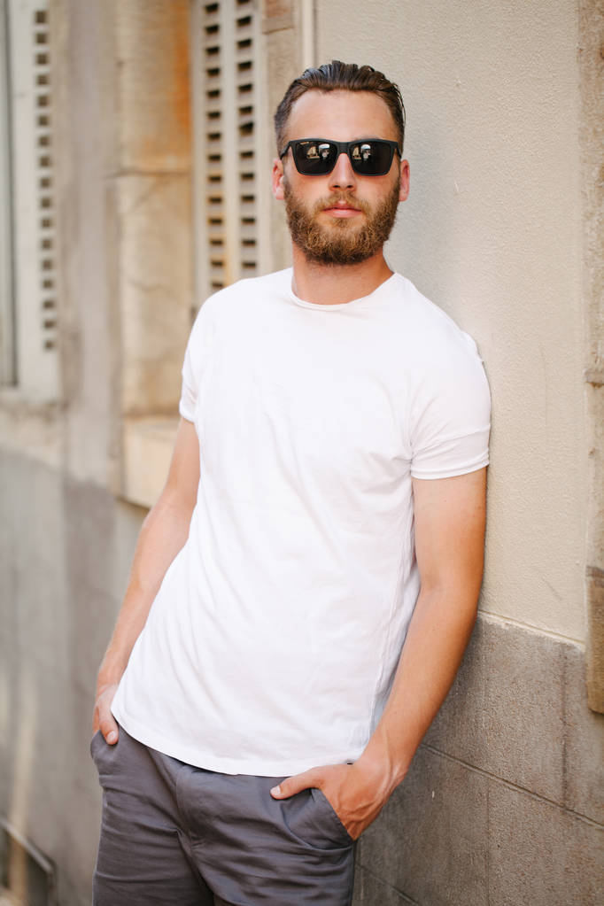 Hipster knappe mannelijke model met baard met witte witte witte t-shirt en een honkbalpet met ruimte voor uw logo of ontwerp in casual stedelijke stijl - Foto, afbeelding